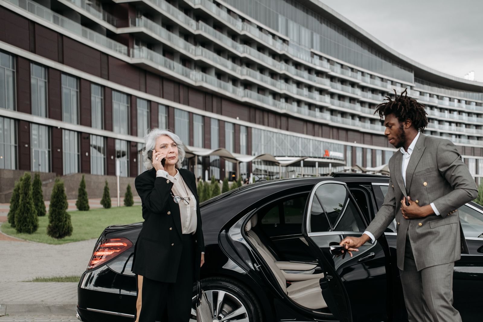 Lux4Rides chauffeur in a suit opening the rear door of a black Mercedes S-Class for a VIP client