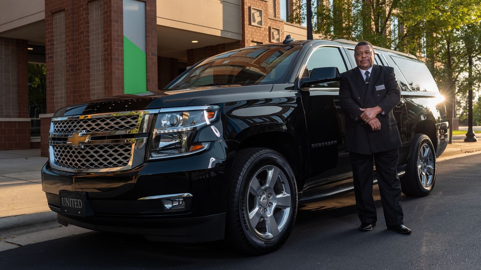 Lux4Rides chauffeur waiting beside a black luxury SUV on standby